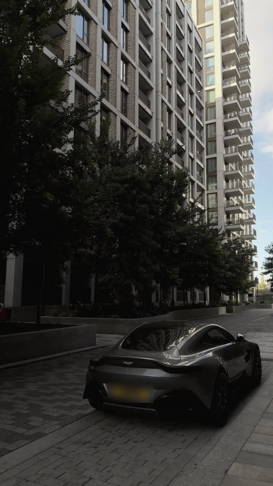 A grey sports car parked beneath a tall residential block