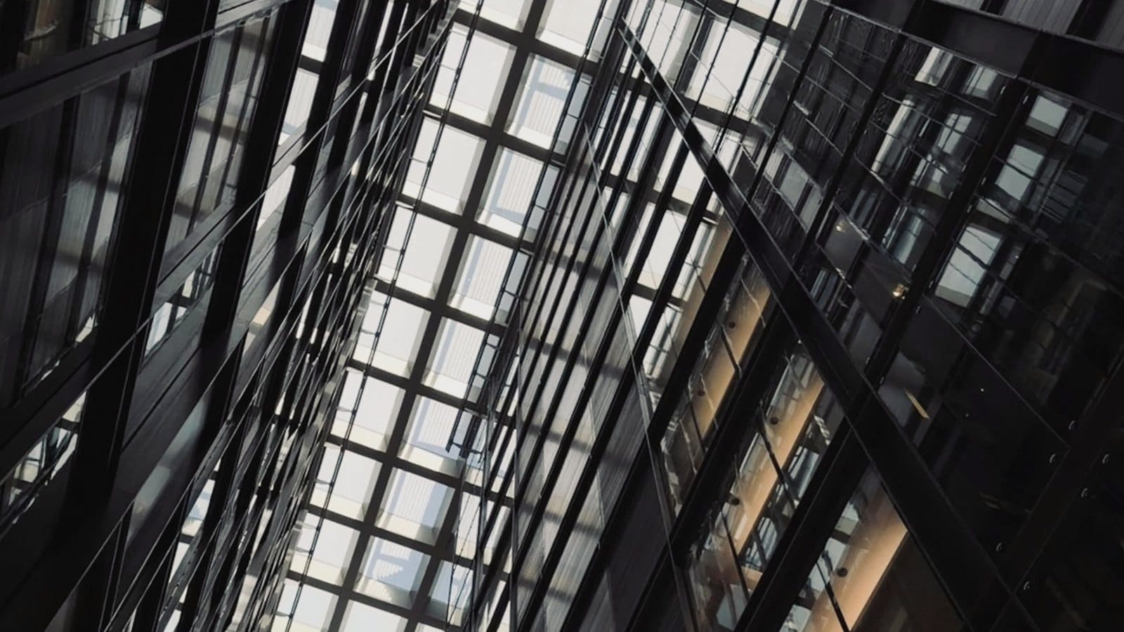 Looking up through a glass atrium roof between dark steel-framed walls