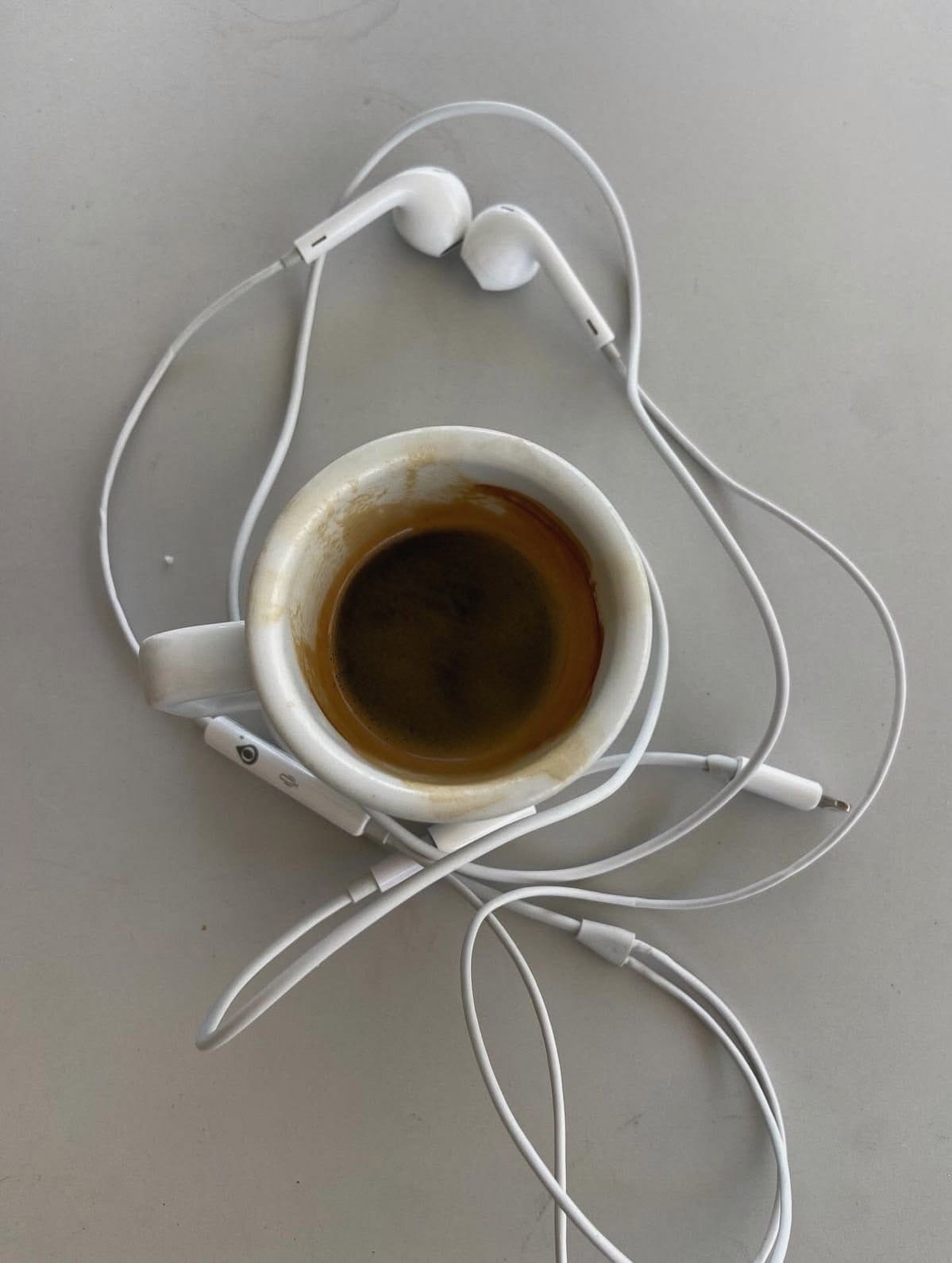 An espresso and a pair of earphones on a grey table, seen from above