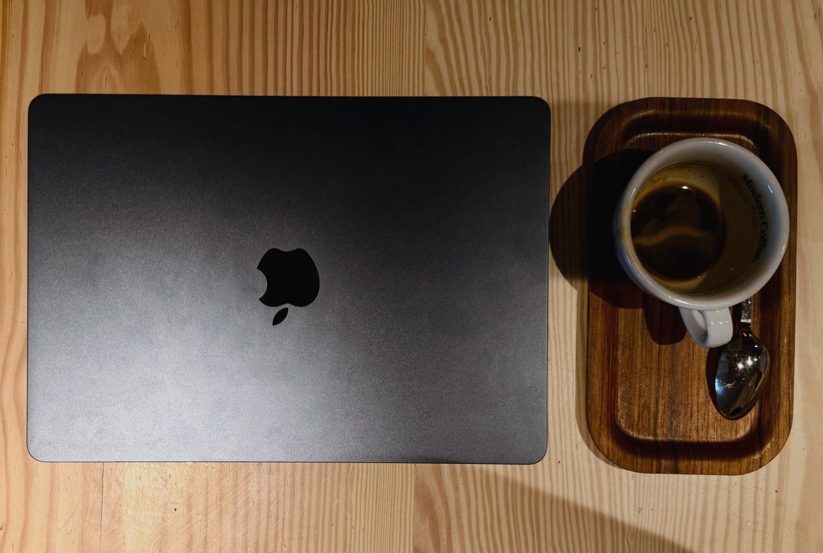 A closed laptop and an espresso on a wooden café table, seen from above