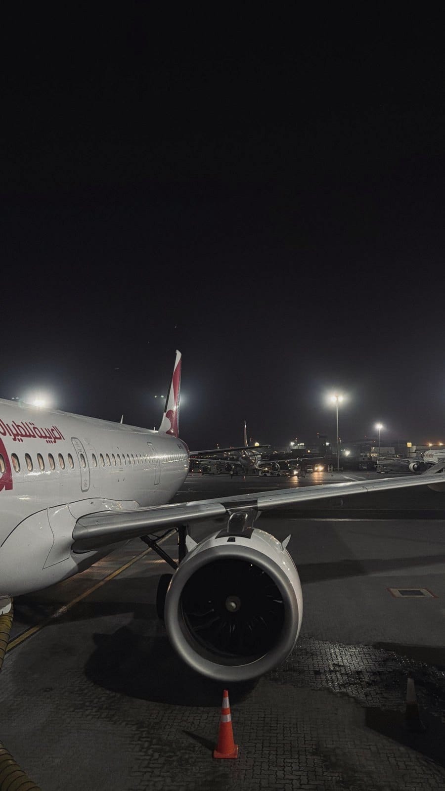 A plane at the gate at night, its engine and wing lit by the apron lights