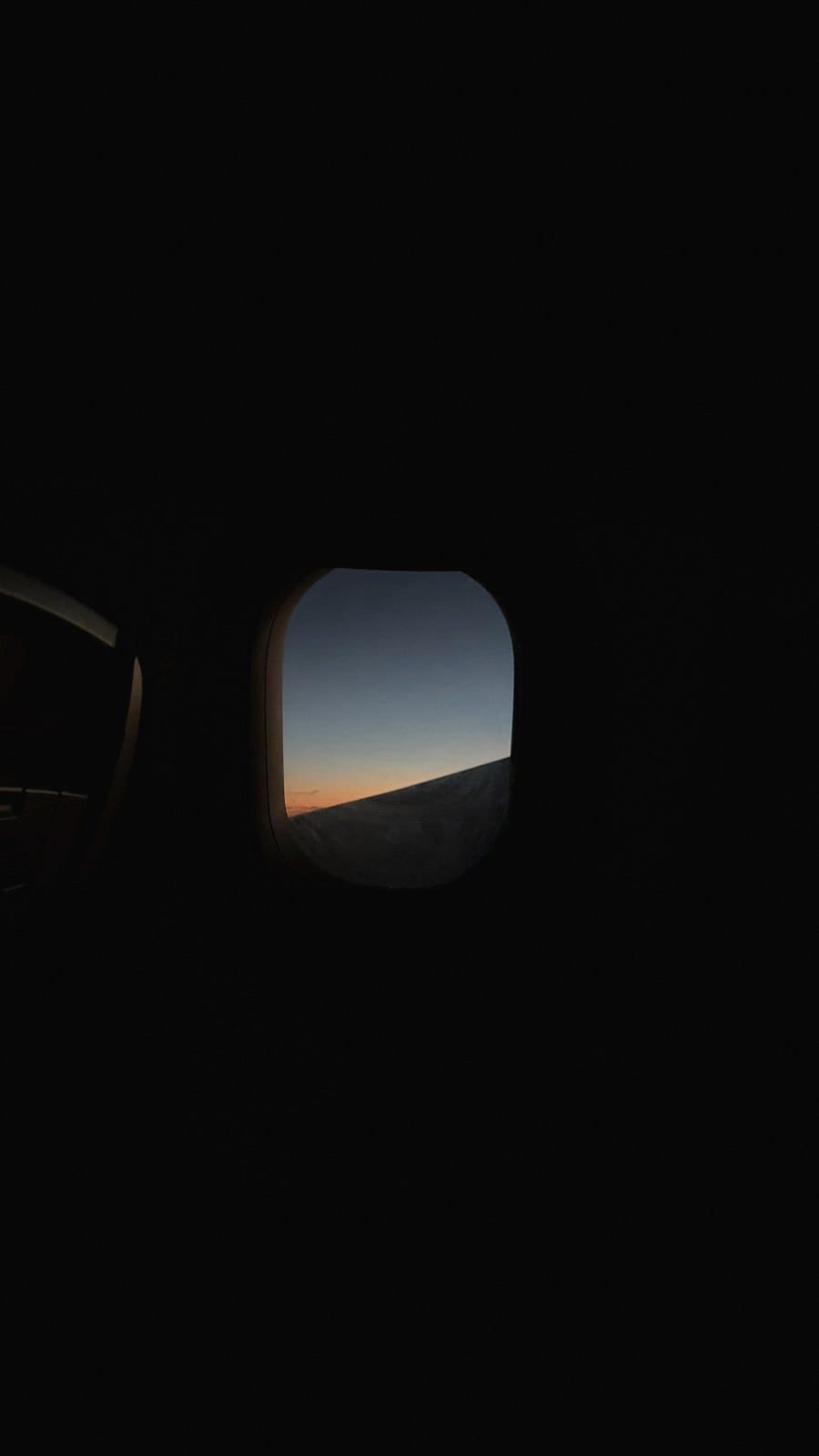 A plane window at dusk, the last orange light on the horizon