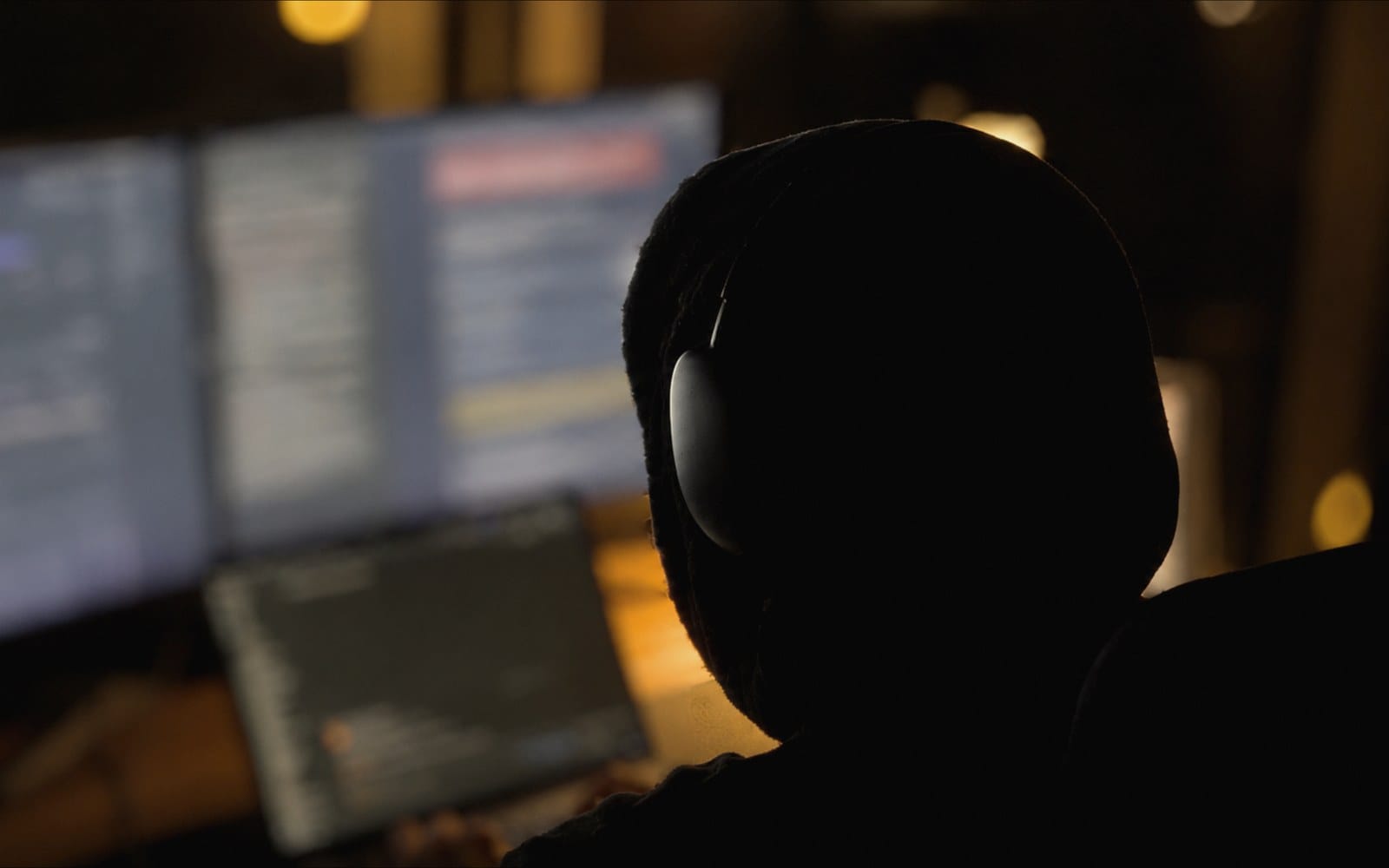 Belal at his desk at night in headphones, working across two monitors and a laptop